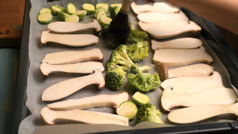 Cogumelos e brócolis de escovadela da mão da mulher com óleo filme