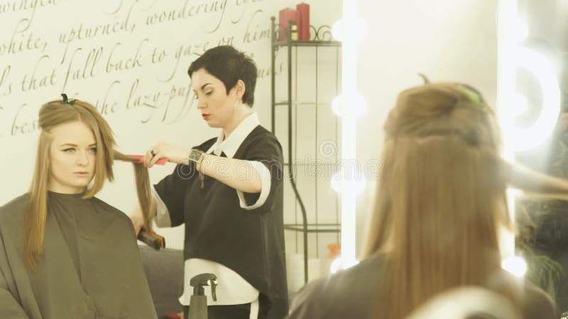 Coiffeur faisant la coiffure avec les pinces et le peigne de cheveux pour des cheveux se redressant dans le salon de beauté Coiff banque de vidéos