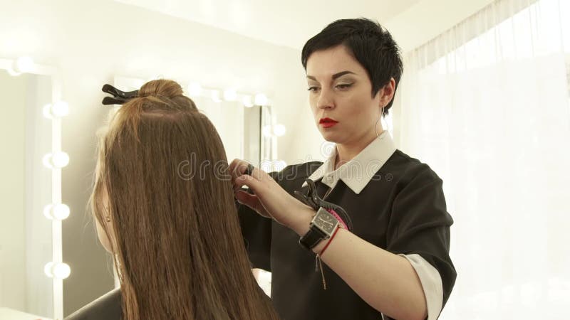 Coiffeur féminin peignant de longs cheveux pour le miroir d'avant de coupe de cheveux de femme dans le salon de beauté Fermez-vou banque de vidéos