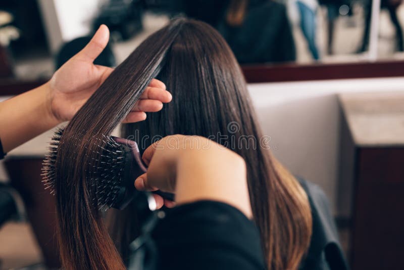 Professional hairdresser styling the hair of a customer at salon. Female hair stylist combing hair using a hair brush. Professional hairdresser styling the hair of a customer at salon. Female hair stylist combing hair using a hair brush.