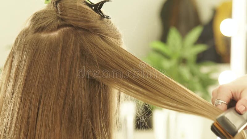 Coiffeur féminin à l'aide des pinces et du peigne de cheveux pour des cheveux se redressant dans le salon de beauté Fermez-vous v clips vidéos