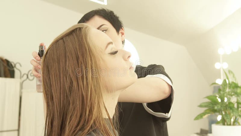 Coiffeur pulvérisant de longs cheveux pour le hairstyling après coupe de cheveux dans le salon de coiffure Hairstyling de femme d banque de vidéos