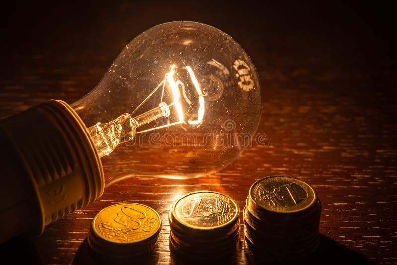 Coins and light bulb on a dark surface stock image