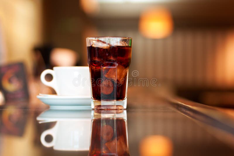 A glass of cola or soda with ice cubes and cup of black coffee on the bar. A glass of cola or soda with ice cubes and cup of black coffee on the bar