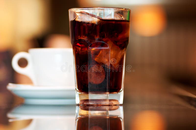 A glass of cola or soda with ice cubes and cup of black coffee on the bar. A glass of cola or soda with ice cubes and cup of black coffee on the bar