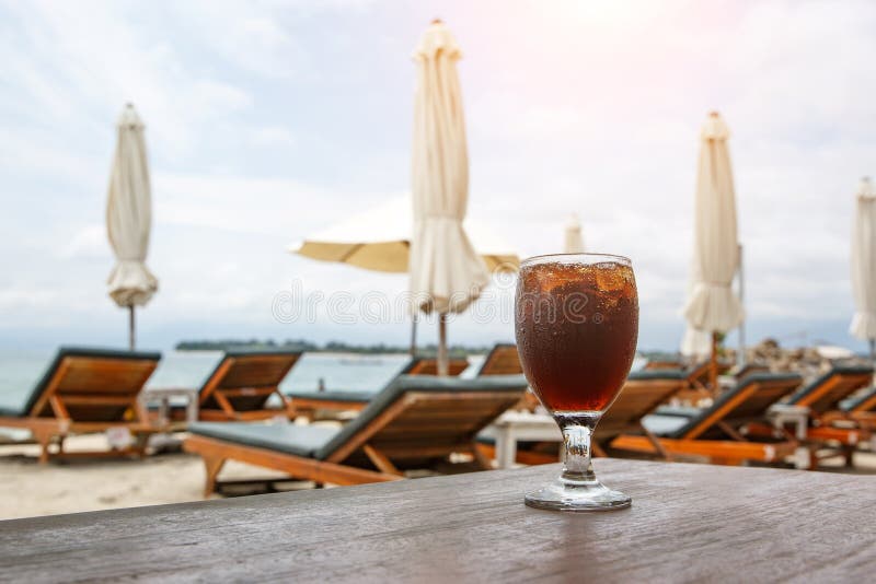 Cola glass on beach with umbrellas. Cooling drink stock photo Cola glass on beach with umbrellas. Cooling drink stock photo