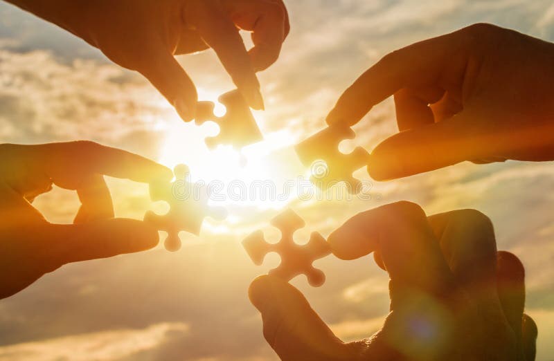 Colaboram quatro mãos que tentam conectar uma parte do enigma com um fundo do por do sol Um enigma à disposição contra a luz sola