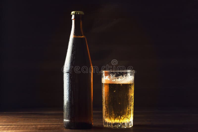 Cold beer bottle and glass with fresh beer in drops of water on dark background, craft brewery royalty free stock image Cold beer bottle and glass with fresh beer in drops of water on dark background, craft brewery royalty free stock image