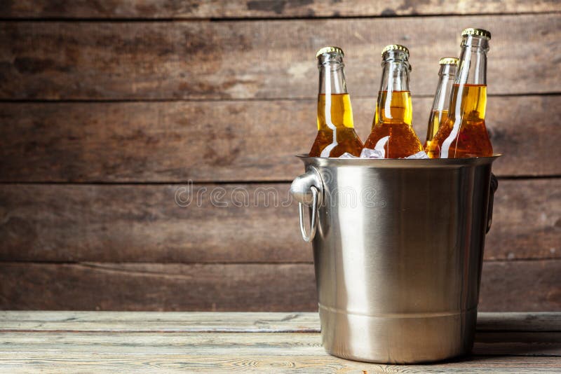 Cold bottles of beer in the bucket on the wooden background