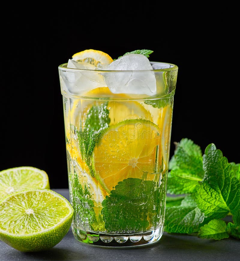 cold drink made from pieces of lemon, lime and leaves of green mint in a glass with water drops