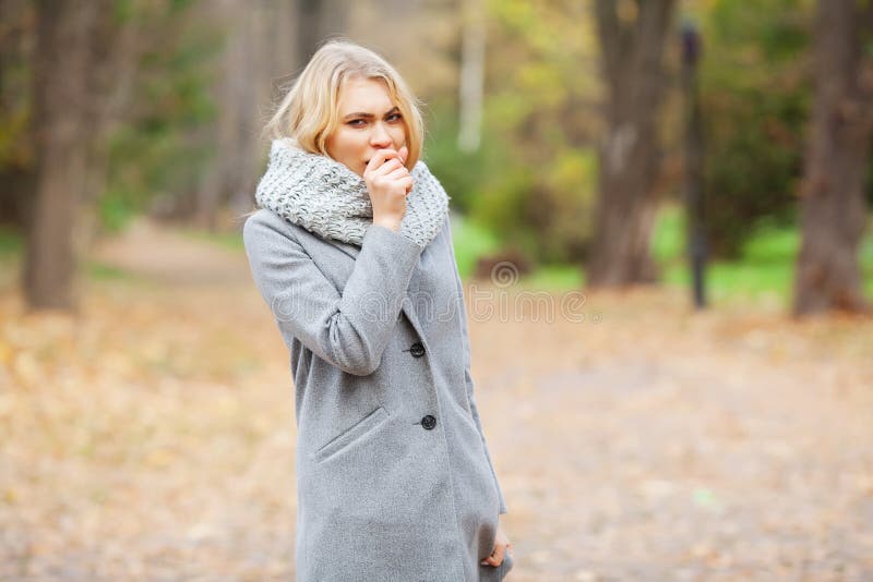 Cold and flu. Young woman in a gray coat walking in the autumn park and warms frozen hand royalty free stock images Cold and flu. Young woman in a gray coat walking in the autumn park and warms frozen hand royalty free stock images