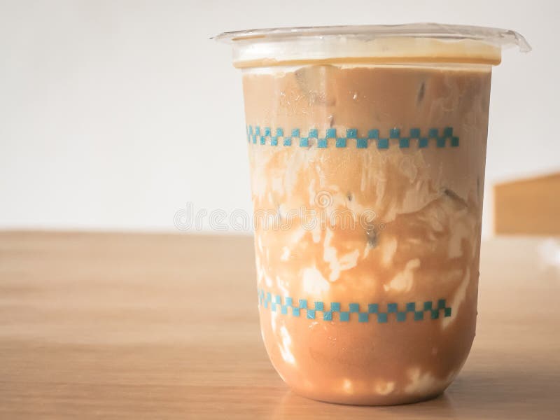 A cold light brown drink in a clear plastic cup on a wooden table with water droplets on the surface. stock photos