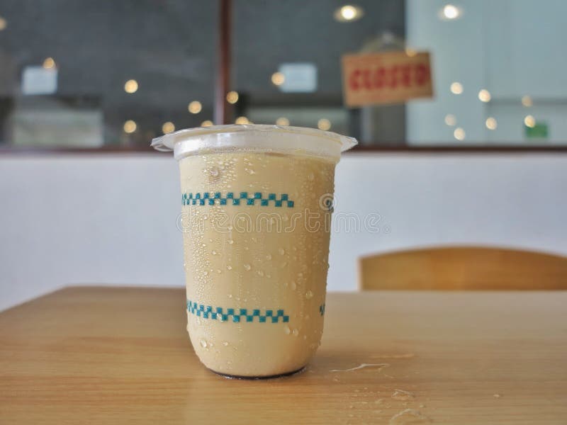 A cold light brown drink in a clear plastic cup on a wooden table with water droplets on the surface. stock images