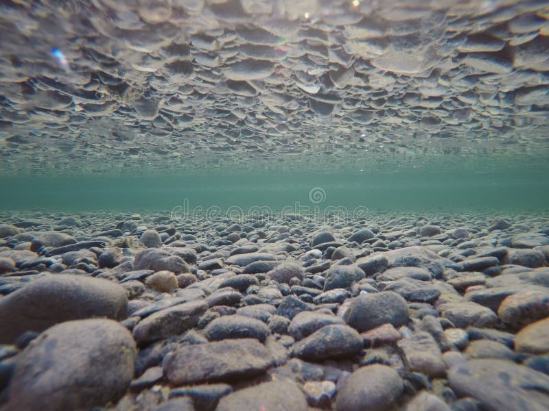 Cold underwater river bed with perfect reflection on surface tension