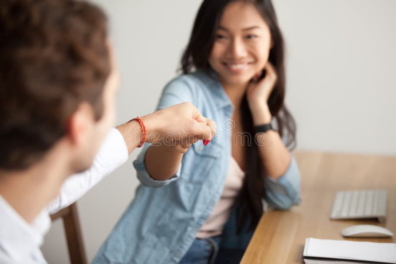 Colega masculino que topa sonriente del puño asiático de la mujer joven en el trabajo imagen de archivo Colega masculino que topa sonriente del puño asiático de la mujer joven en el trabajo imagen de archivo