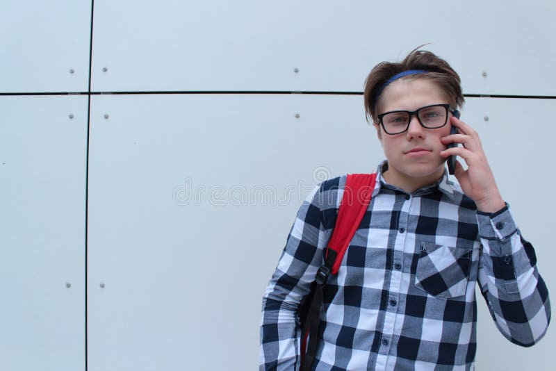 Colegial o estudiante del adolescente del muchacho en la camisa, sonriendo con los vidrios, mochila roja imagen de archivo libre de regalías Colegial o estudiante del adolescente del muchacho en la camisa, sonriendo con los vidrios, mochila roja imagen de archivo libre de regalías