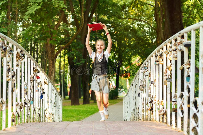 Colegiala del estudiante feliz con las coletas en uniforme con los libros en manos sobre el brid principal de los funcionamientos imagenes de archivo Colegiala del estudiante feliz con las coletas en uniforme con los libros en manos sobre el brid principal de los funcionamientos imagenes de archivo