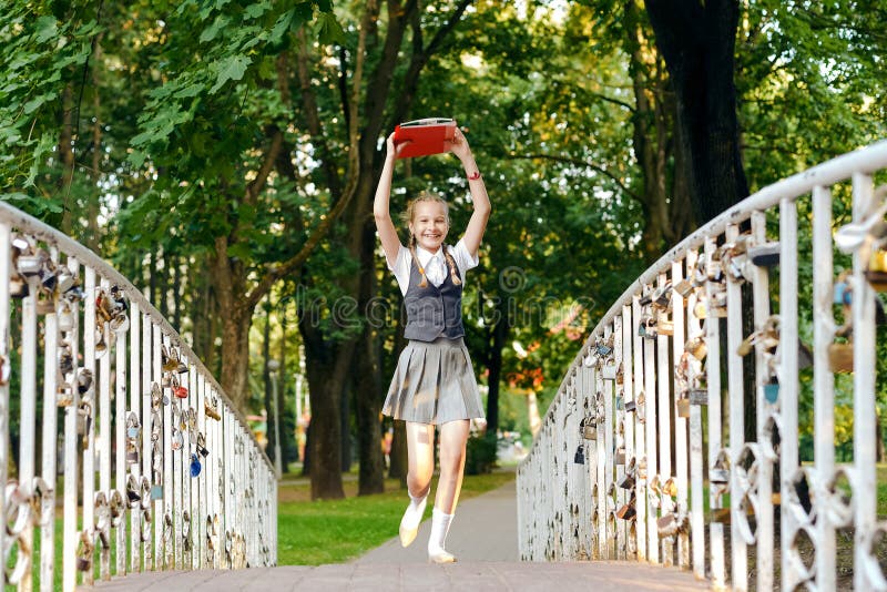 Colegiala del estudiante feliz con las coletas en uniforme con los libros en manos sobre el brid principal de los funcionamientos fotografía de archivo libre de regalías Colegiala del estudiante feliz con las coletas en uniforme con los libros en manos sobre el brid principal de los funcionamientos fotografía de archivo libre de regalías