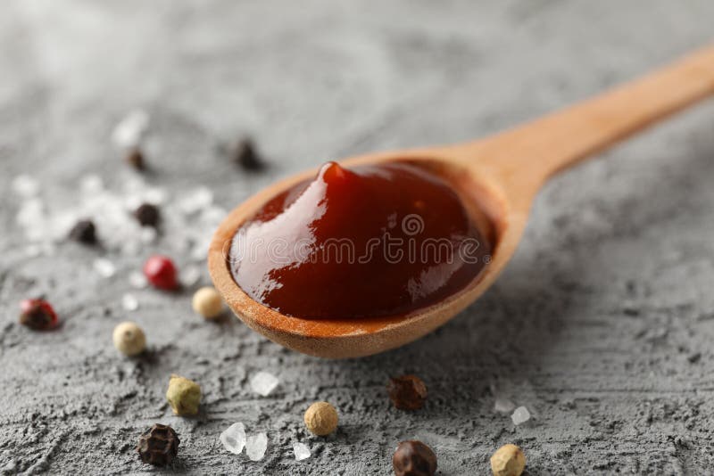 Spoon of delicious barbeque sauce, ingredients on grey background, space for text. Closeup. Spoon of delicious barbeque sauce, ingredients on grey background, space for text. Closeup