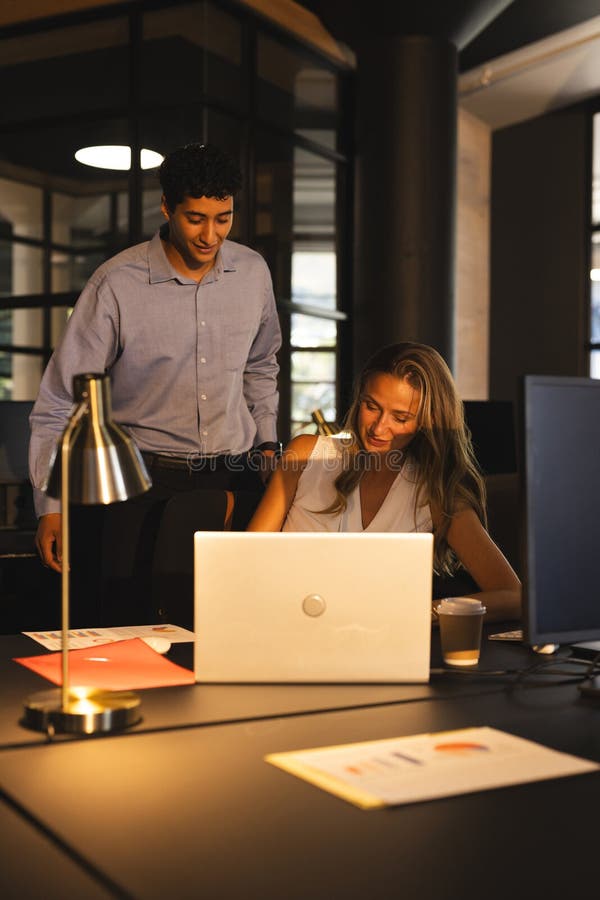 Colleagues collaborating on laptop in modern office during late-night work session stock photography