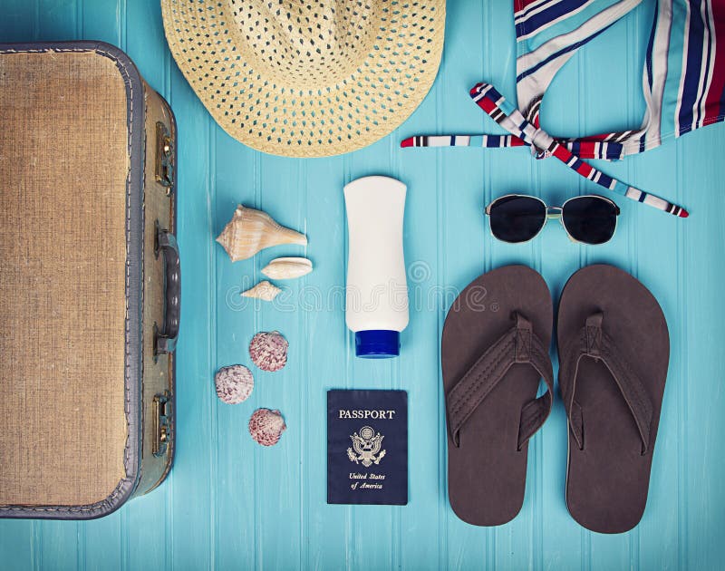 A collection of travel items including suitcase, passport, sandals, sunglasses, swim suit, sunscreen and straw hat on turquoise background