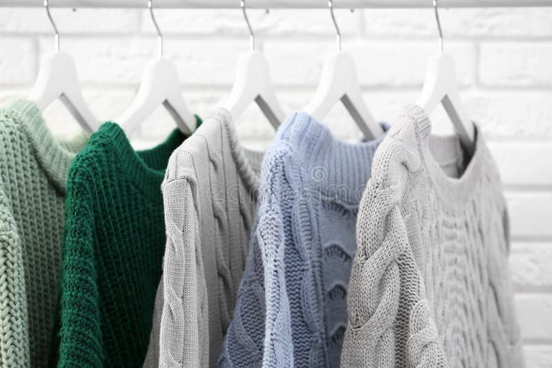 Collection of Warm Sweaters Hanging on Rack Near Wall, Closeup Stock ...