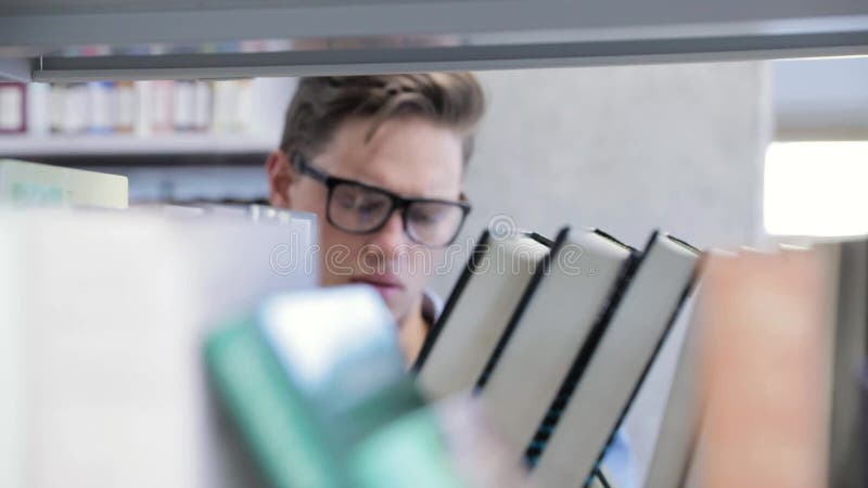 Collegebibliothek Männlicher Student, der nach Buch auf Bücherregalen sucht