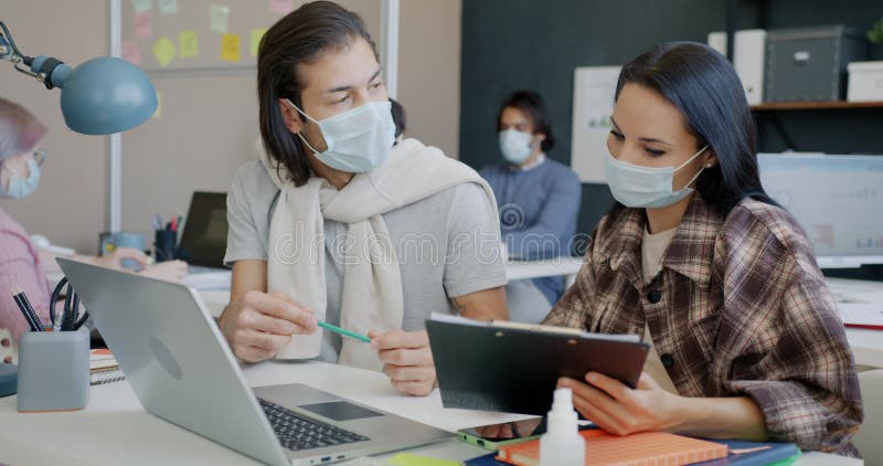 Colleghi e colleghi che lavorano con il laptop e parlano indossando mascherine per la faccia in ufficio