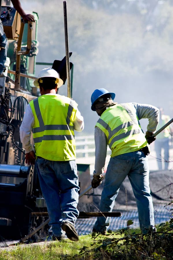 Two men working alongside an asphalt paving machine. Two men working alongside an asphalt paving machine.