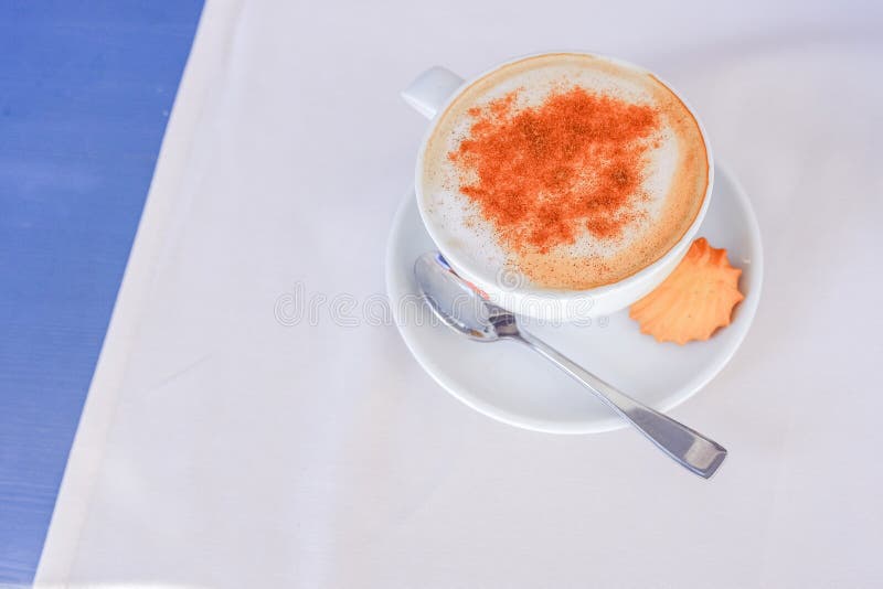 Color de Brown de la canela en polvo en la nata montada escarchada de la taza del capuchino en la taza de cerámica blanca en la t imágenes de archivo libres de regalías Color de Brown de la canela en polvo en la nata montada escarchada de la taza del capuchino en la taza de cerámica blanca en la t imágenes de archivo libres de regalías