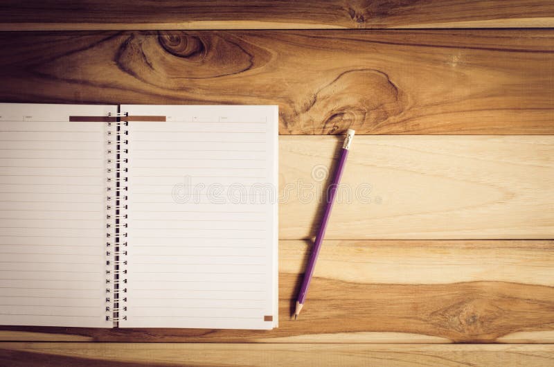 Color pencils in the cups and notebook placed on a desk.