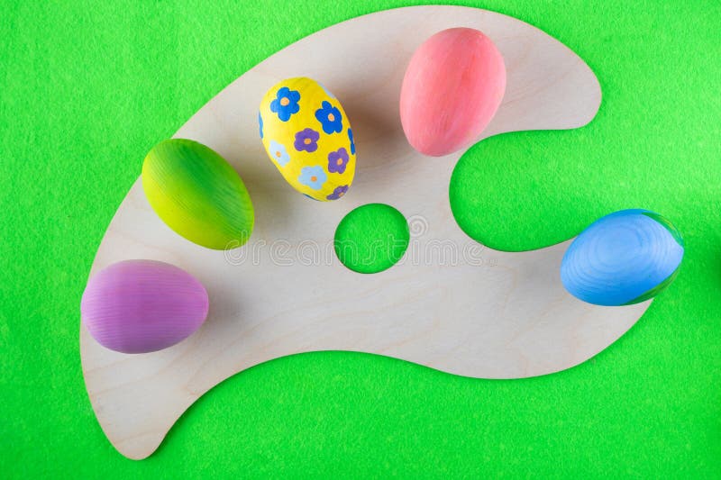 Colored Easter eggs lay on wooden art palette on green backdrop. Top view, flat lay. Creative happy easter concept