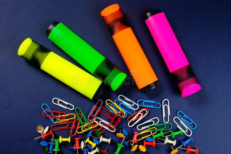 Colored paper clips, button and markers on a dark blue background. stock image