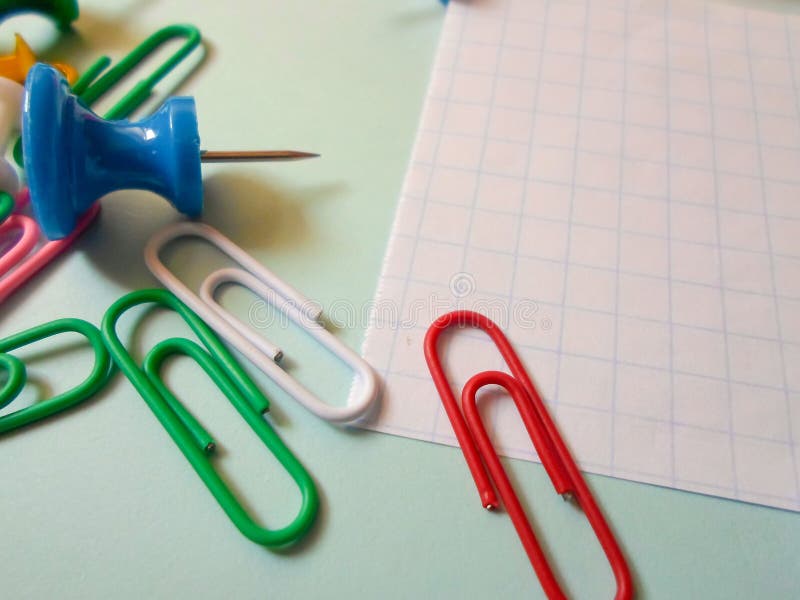 Colored Paper Clips and Pins on a White Sheet of Paper are Scattered