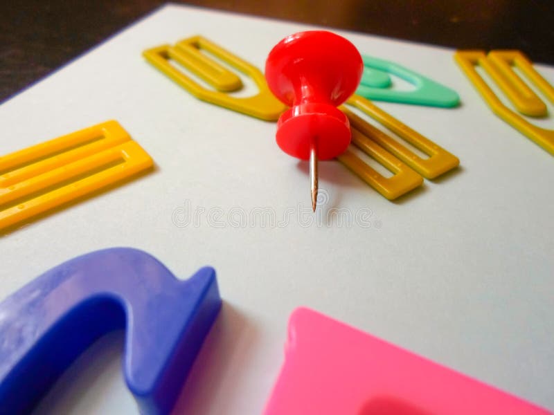 Colored Paper Clips and Pins on a White Sheet of Paper are Scattered