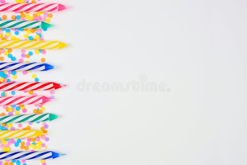 Colorful birthday cake candles with candy sprinkles. Above view side border on a white background. Copy space. Colorful birthday cake candles with candy sprinkles. Above view side border on a white background. Copy space