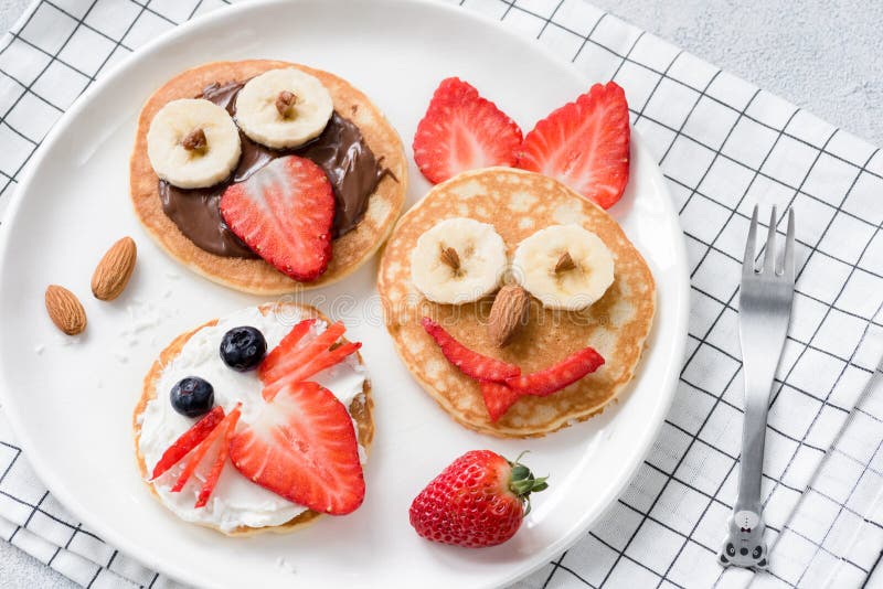 Colorful breakfast meal for kids. Pancake food art, funny animal faces made with fruits, nuts and chocolate spread