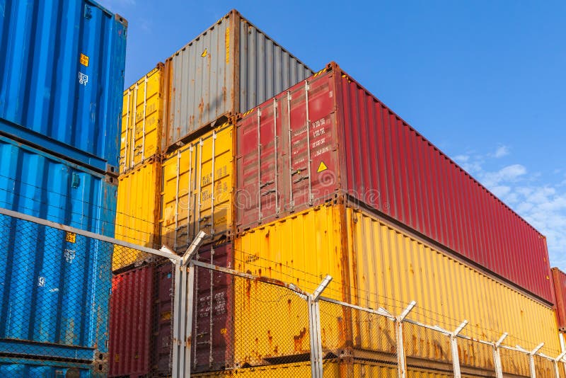 Colorful Industrial cargo containers are stacked behind metal fence with barbed wire. Colorful Industrial cargo containers are stacked behind metal fence with barbed wire