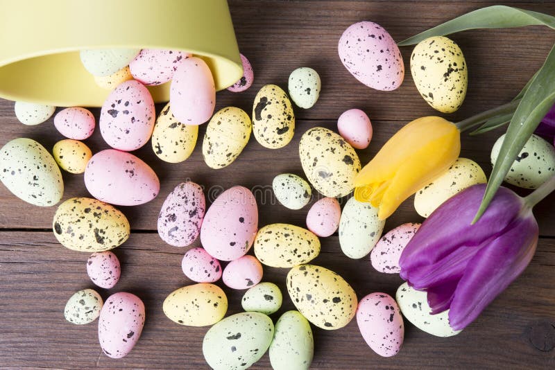 Colorful Easter eggs on bowl and tulips on a wooden table