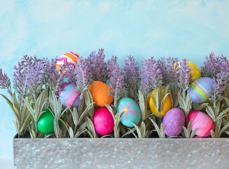 Colorful Easter Eggs Still Life Display with Lavender Flowers in Metal Planter against Blue Sky Background