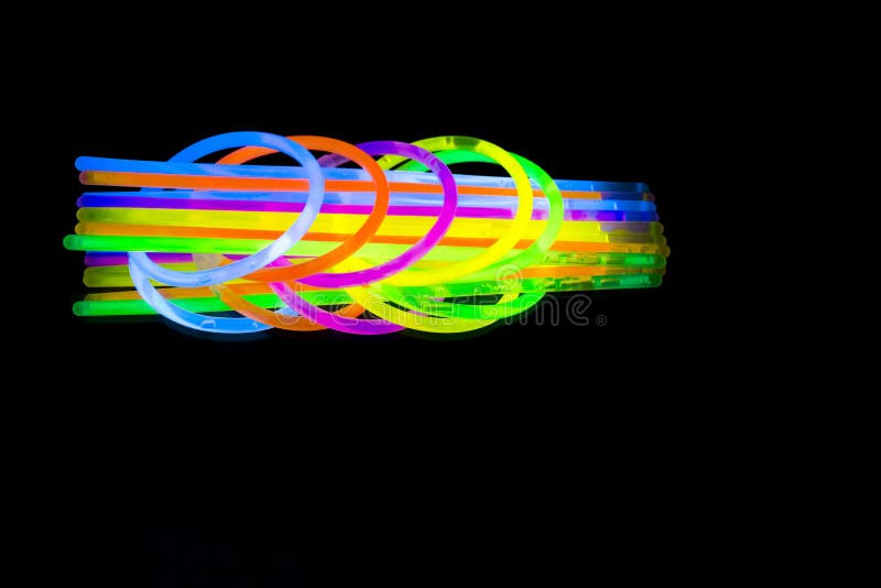 Colorful fluorescent light neon glow stick bracelet strap wristband and tubes on mirror reflection black background