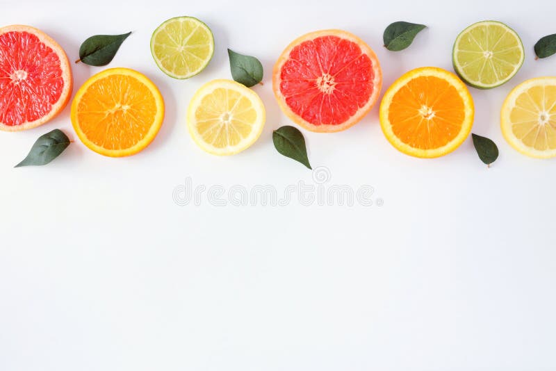 Colorful fruit border of fresh citrus slices with leaves. Top view, flay lay over a white background with copy space stock image