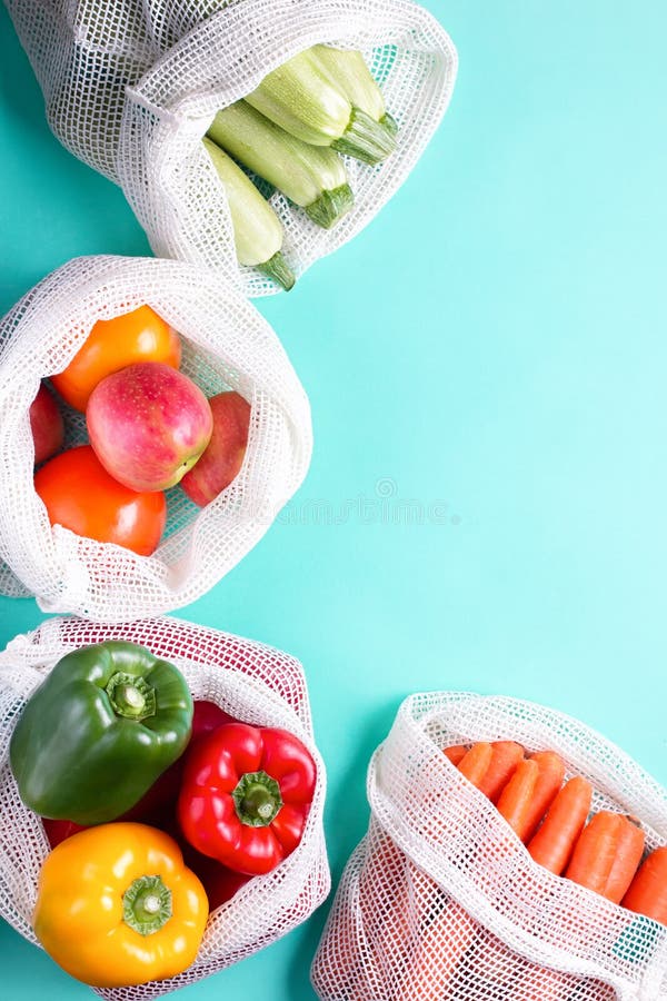 Colorful fresh fruits and vegetables in reusable cotton bags on blue background. Zero waste or responsible food shopping and