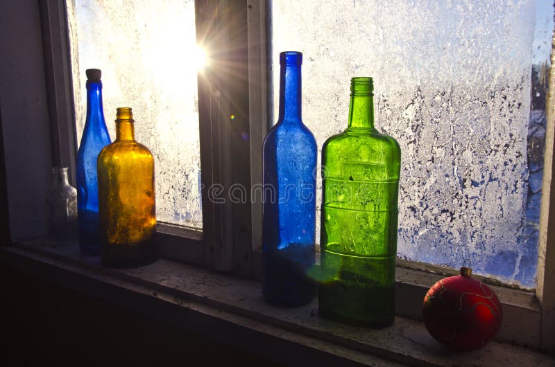 Colorful glass bottles on winter old farm window with hoarfrost ice