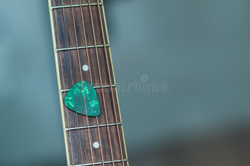 Colorful green guitar pick on finger board.