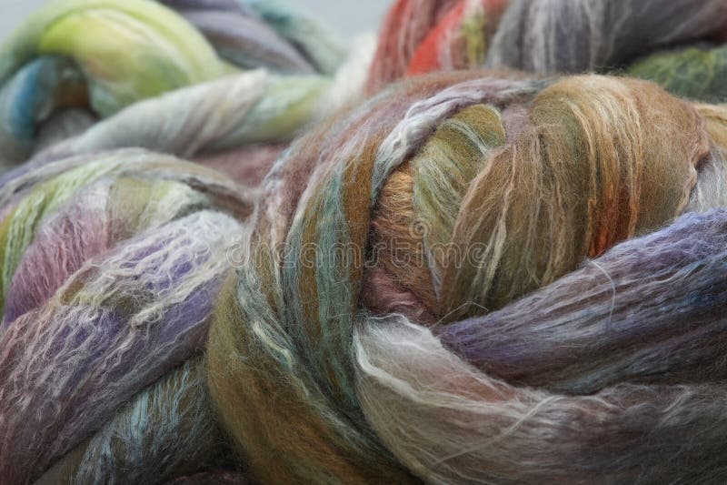 Colorful, handdyed roving of sheepwool, braid and rolled up, natural material ready for spinning on a traditional spinning wheel as a hobby.