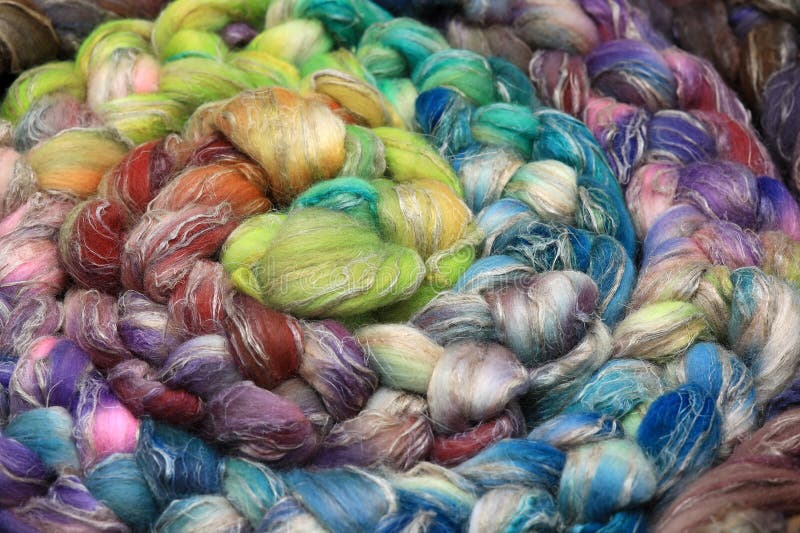 Colorful, handdyed roving of sheepwool, braid and rolled up, natural material ready for spinning on a traditional spinning wheel as a hobby.