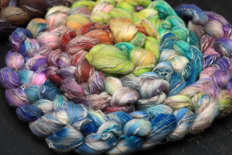 Colorful, handdyed roving of sheepwool, braid and rolled up, natural material ready for spinning on a traditional spinning wheel as a hobby.