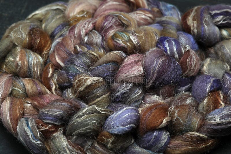 Colorful, handdyed roving of sheepwool, braid and rolled up, natural material ready for spinning on a traditional spinning wheel as a hobby.