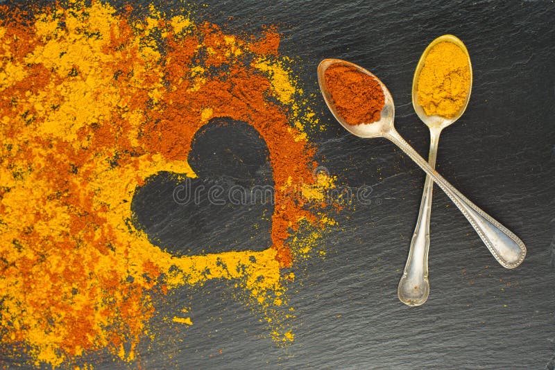 Colorful heart from spices with two vintage spoons on black background with two vintage spoons. Selective focus. Valentines day.